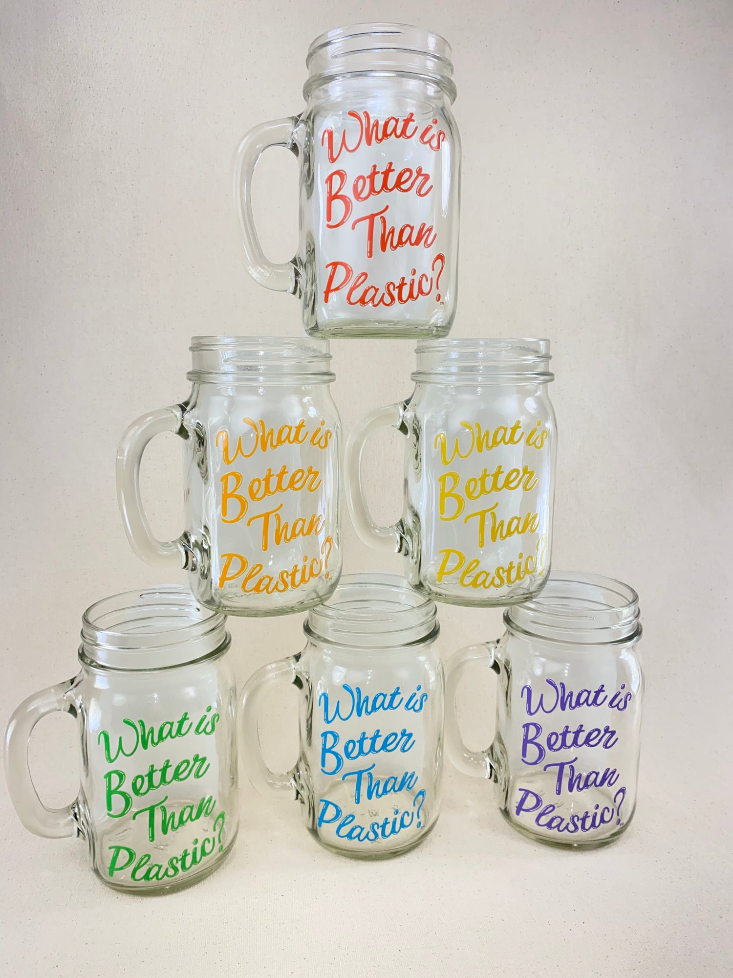 White background with stacked pyramid of glass drinking mason jars each with a different rainbow spectrum color logo “What is Better Than Plastic?”